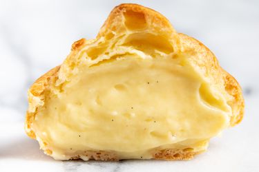 A choux pastry puff filled with pastry cream, cut in half so you can see the vanilla pastry cream
