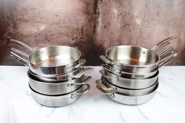 nine different saute pans on a marble counter in two stacks