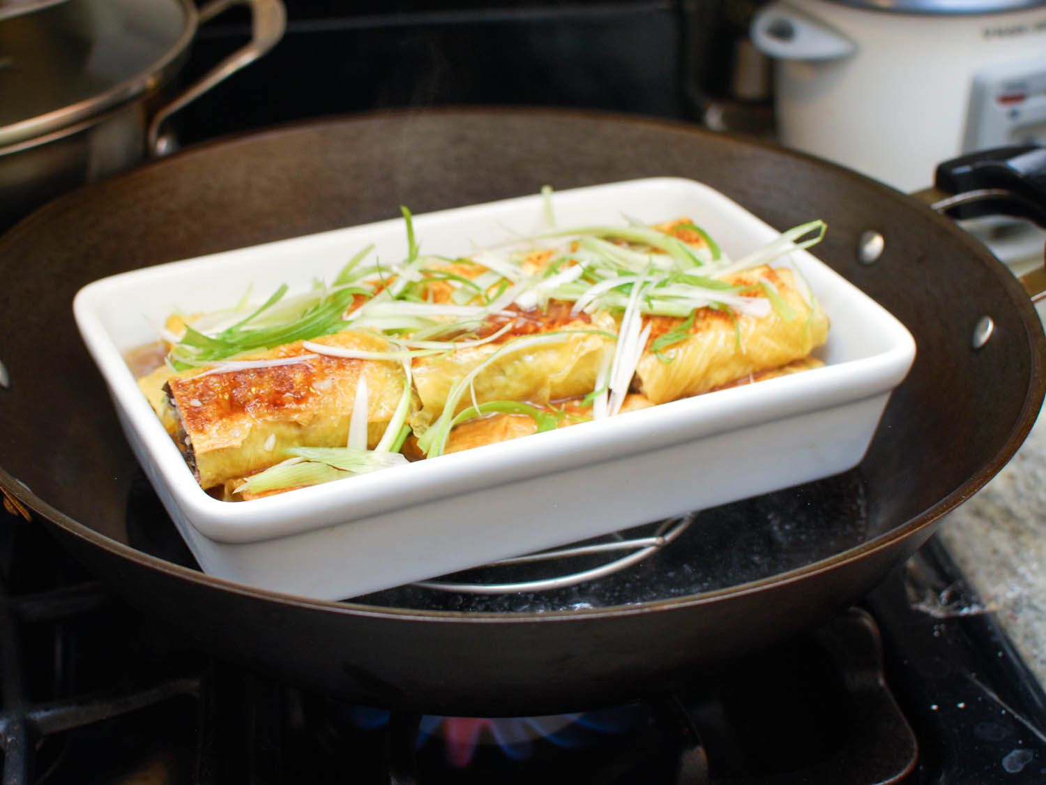 将装满豆腐卷、高汤和葱花的烤盘放在锅内的架子上，准备蒸。