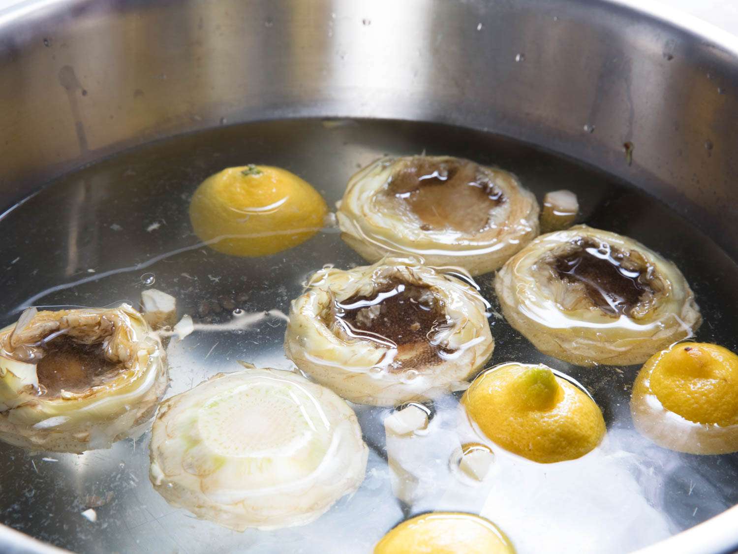 将清洗干净的洋蓟心和柠檬半块漂浮在一个金属碗里。