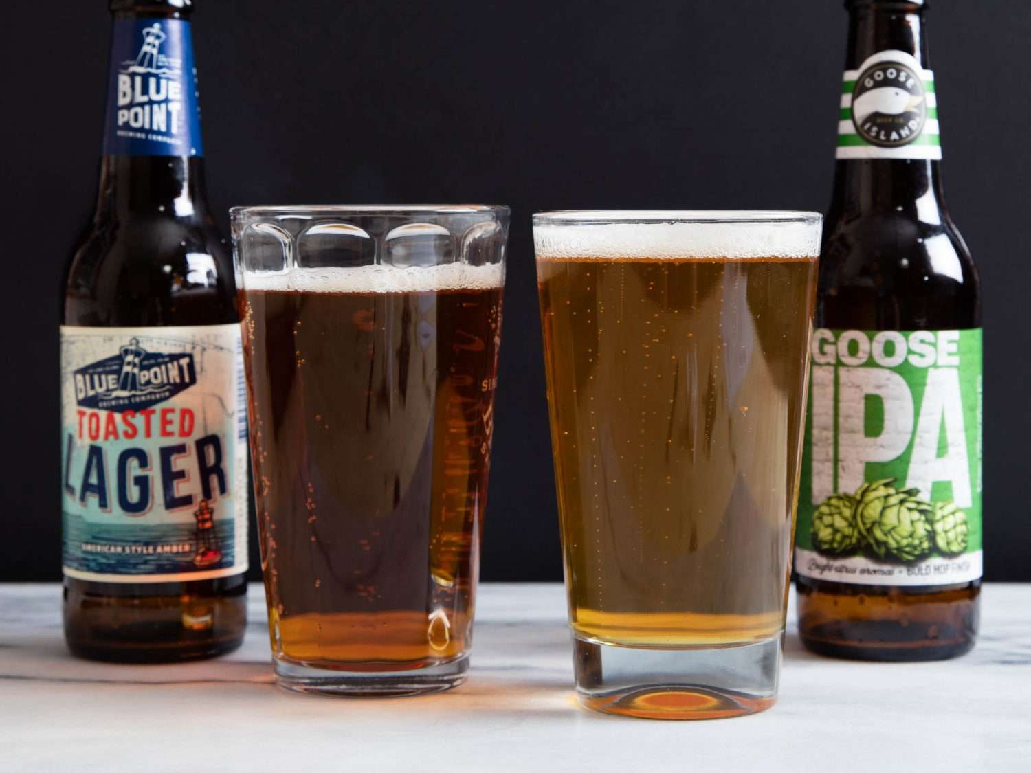 一种拉格啤酒和一种印度淡啤酒，分别倒入玻璃杯中，瓶子放在啤酒旁边。