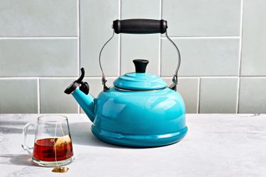 a blue tea kettle on a marble surface with a mug of tea beside it