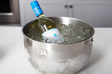 A bottle of wine chilling in heavily iced water in a stainless mixing bowl.