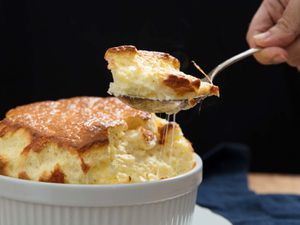 一种大而美味的奶酪蛋奶酥，有人在砂锅上举着一勺蛋奶酥。