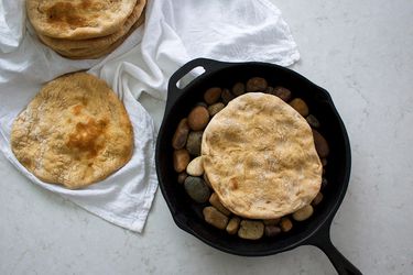 Taboon breads in a cast-iron skillet on river pebbles and spread out across a white linen.