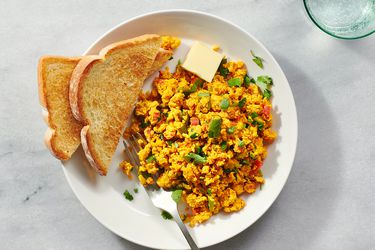 The anda bhurji on a white ceramic plate with toasted white bread and a pat of butter on a stone counter
