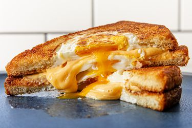 两半烤奶酪蛋洞三明治摞在一起，奶酪和鸡蛋从中间溢出来。