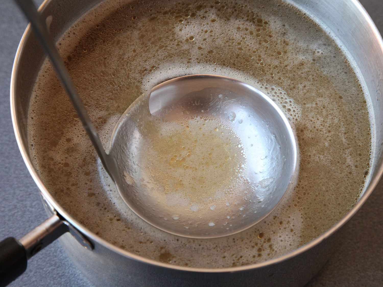 用勺子撇去高压锅越南河粉汤顶部的杂质。
