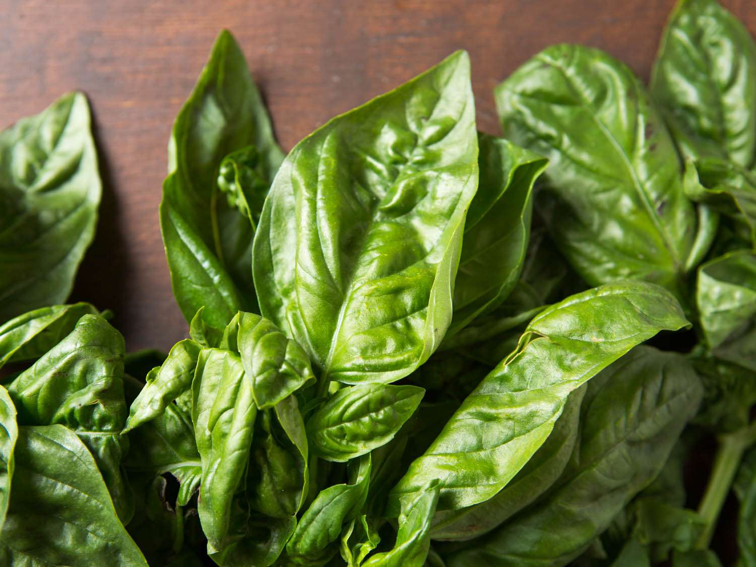A close-up photograph of bunches of fresh basil leaves on a wooden cutting board.