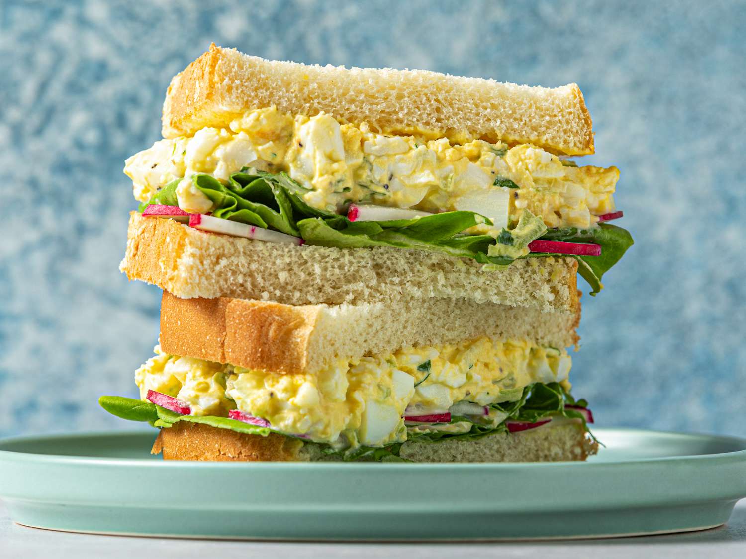鸡蛋沙拉三明治，切成两半，两半叠在一起。三明治里有鸡蛋沙拉、黄油生菜和切成薄片的萝卜。