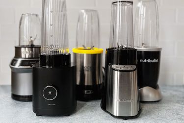 five personal blenders on a countertop with white tile background