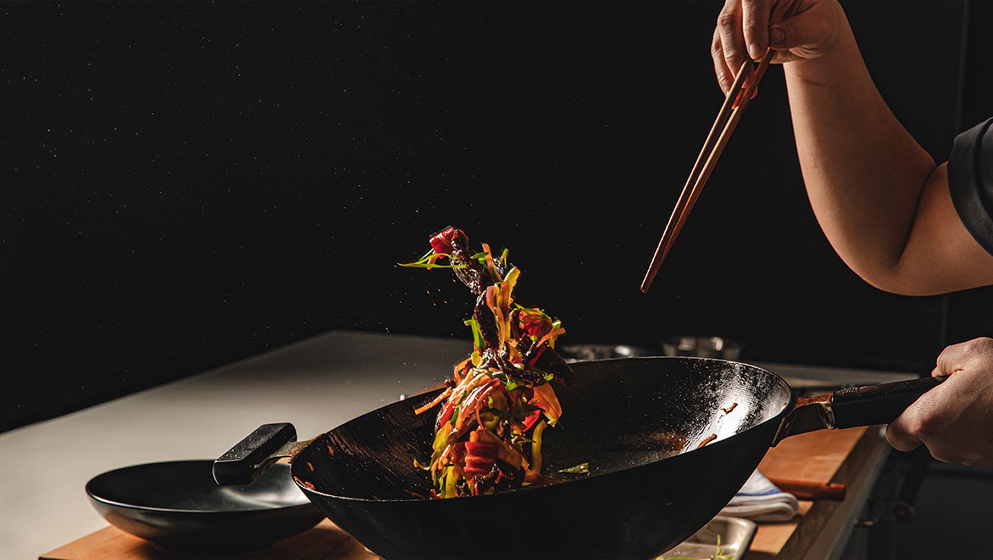 丰富多彩的食物悬浮在空气造成一个人扔一段时间拿着筷子在一个黑暗的厨房。