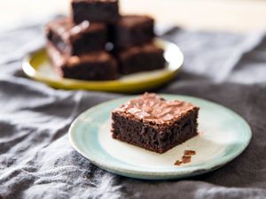 一个有光泽的软糖巧克力布朗尼放在一个小盘子里，背景是一堆布朗尼。