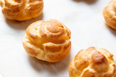 Freshly baked choux pastry puffs on a parchment lined baking sheet.