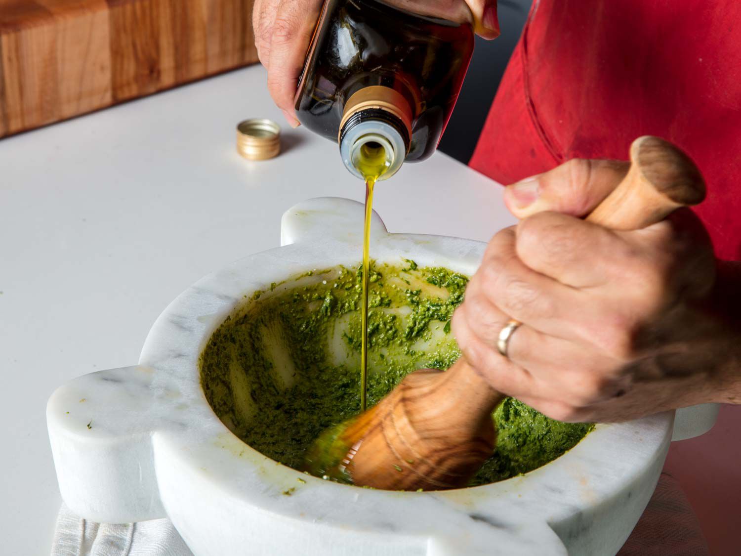 Drizzling olive oil into basil, pine nut, and garlic paste in a marble mortar to make into traditional pesto sauce.