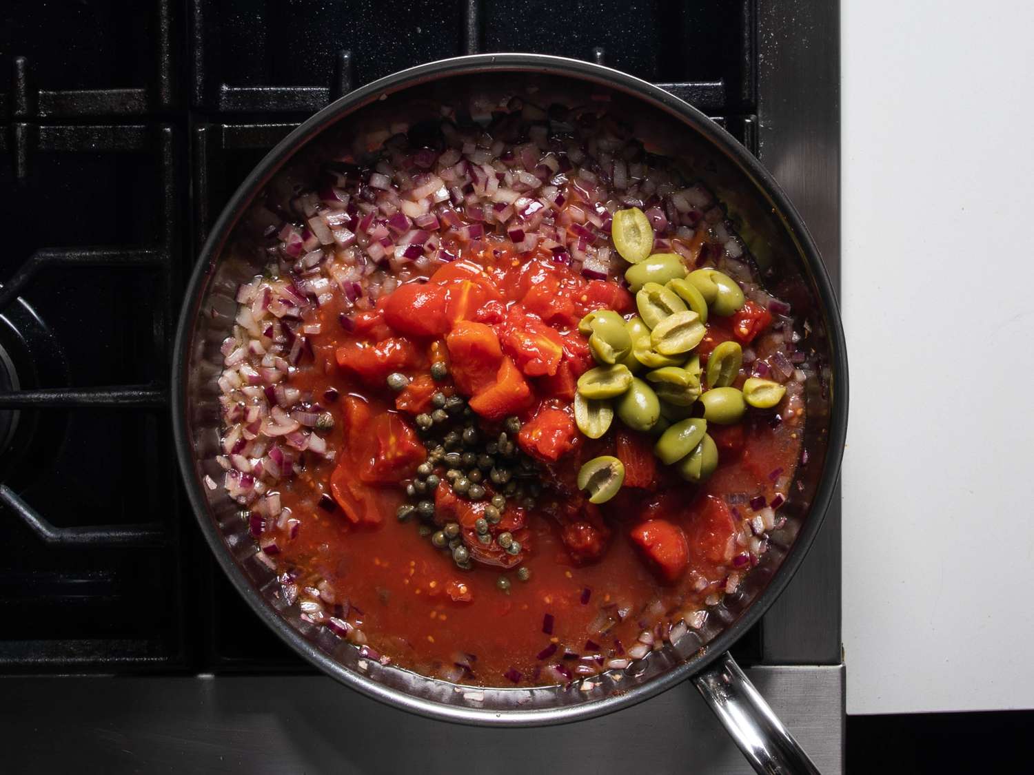 番茄块和果汁,橄榄和酸豆已经被添加到锅的sautA©ed洋葱,就在搅拌在一起。