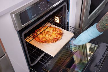 一只戴着烤箱手套的手从烤箱里拉出一块烤石，上面有一块披萨