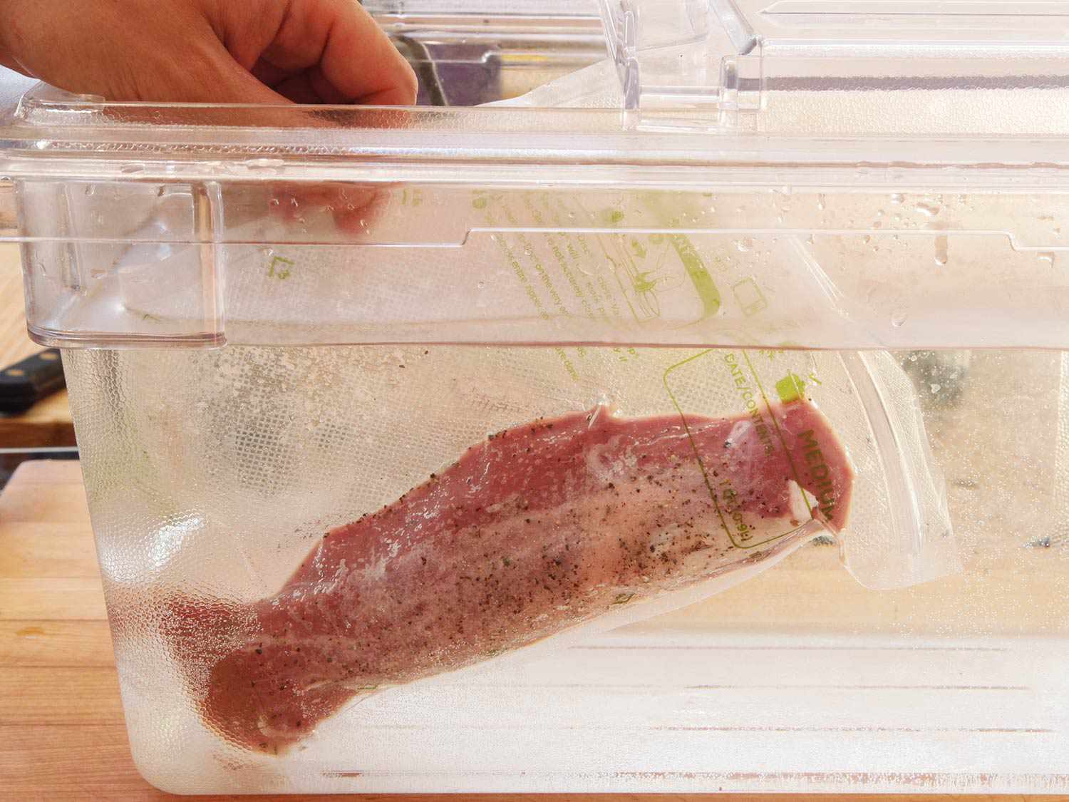 Adding vacuum sealed pork tenderloin to a water bath to cook sous vide.