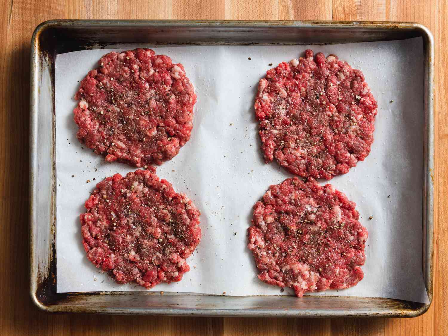4 beef patties formed and seasoned on a baking sheet