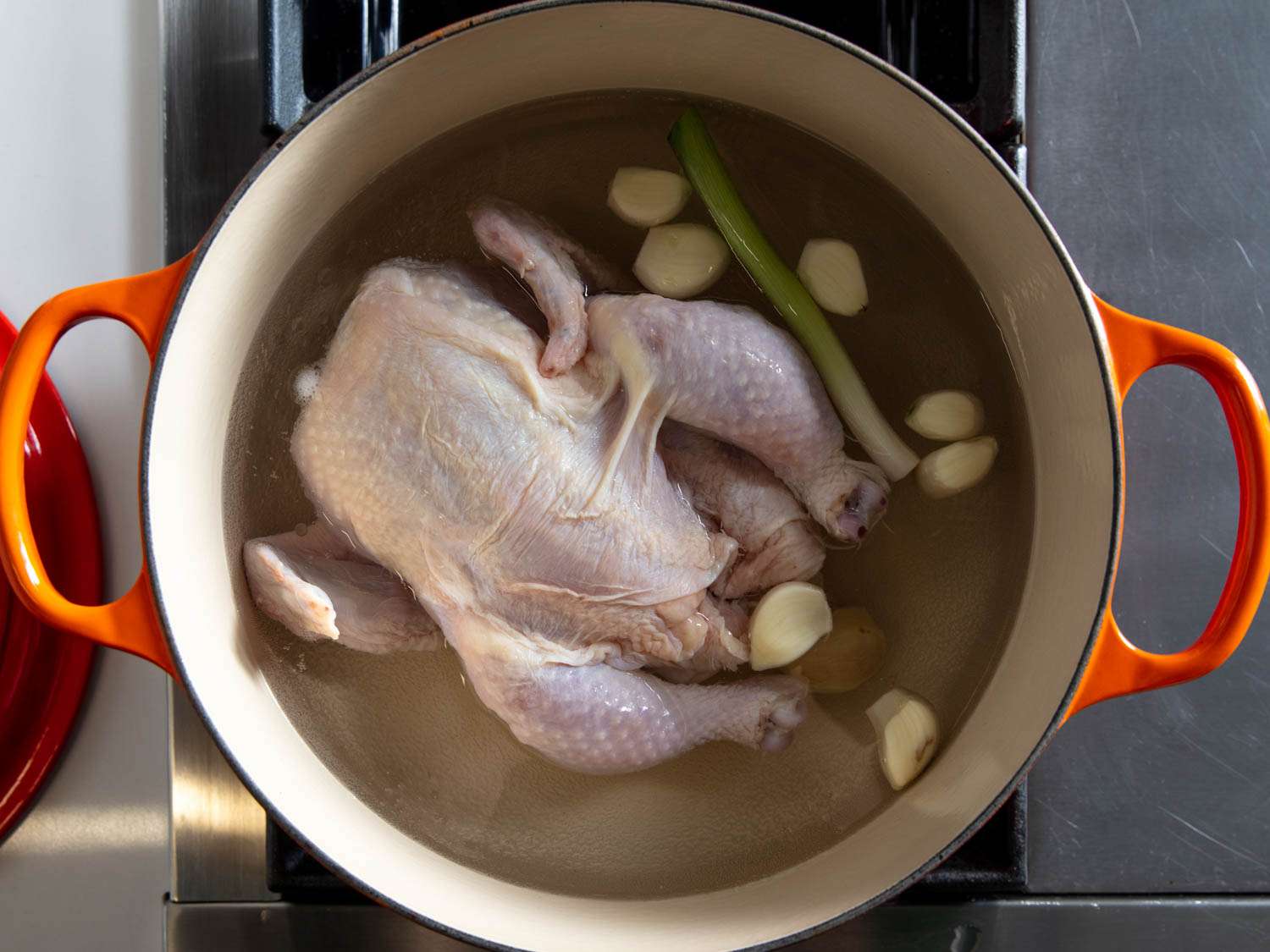 A whole raw chicken in a pot with water, garlic, and green onion