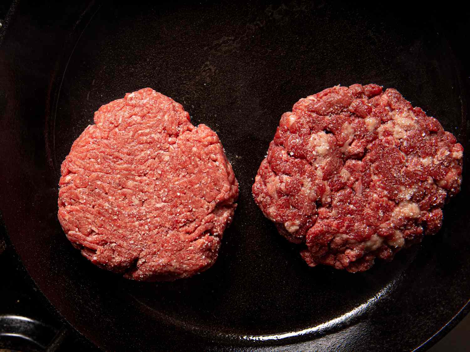 One normal beef burger and one waygu burger side by side in a pan