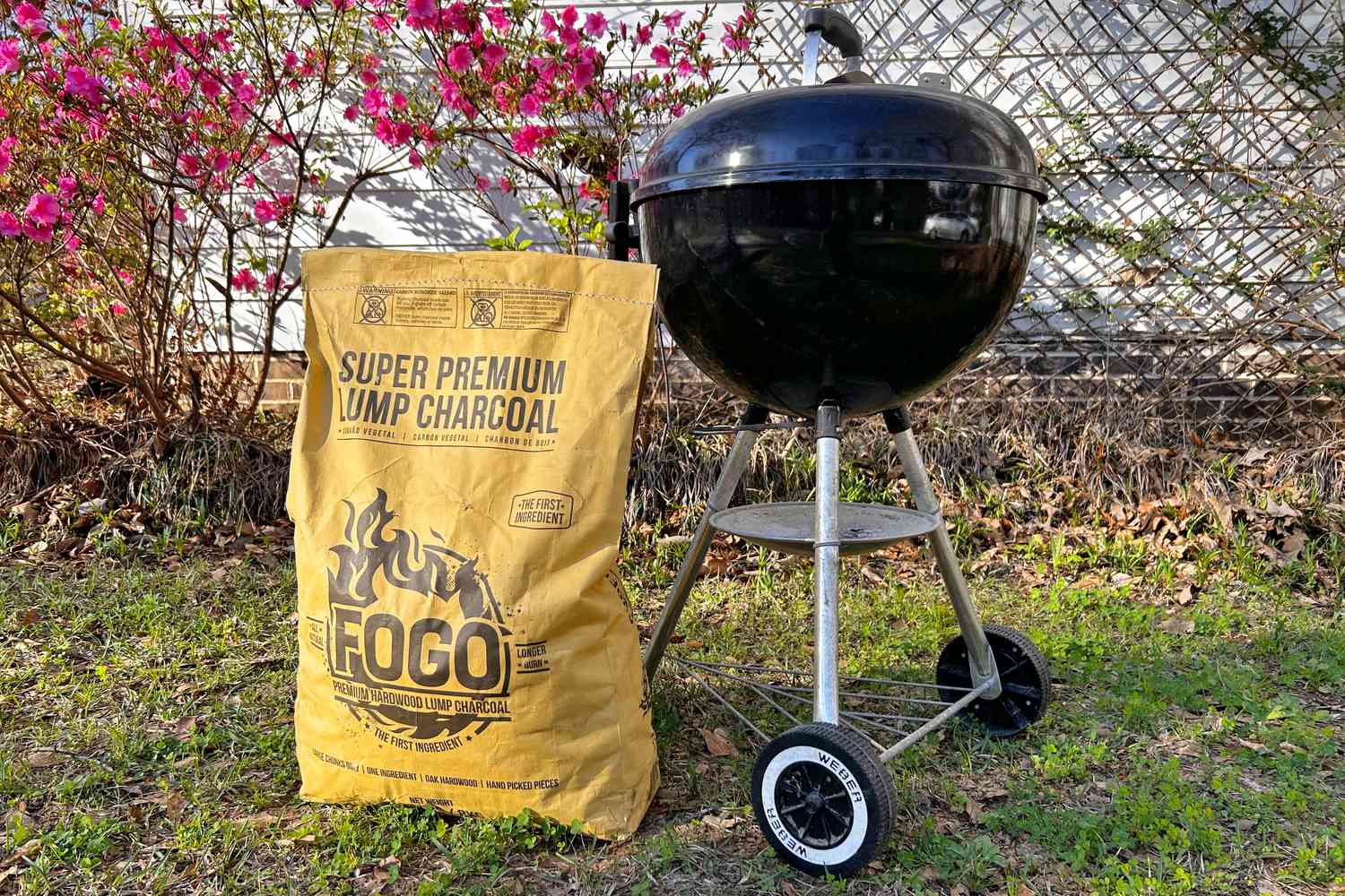 a yellow bag of lump charcoal beside a charcoal grill