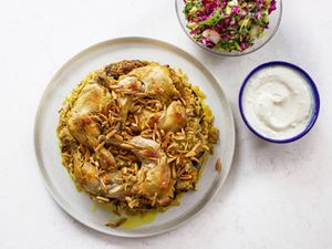 Maqlubeh被镀在一个白色的盘子上，旁边有一碗酱汁和一小份沙拉