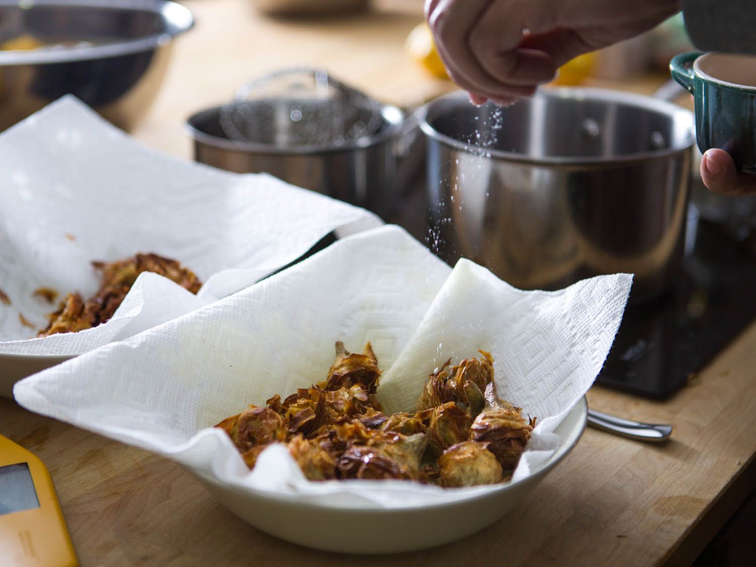 把盐撒在炸过的洋蓟心上，沥干后放在铺着纸巾的碗里。