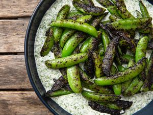 Charcoal Chimney–Grilled Sugar Snap Peas in a bowl on top of Buttermilk-Dill Dressing