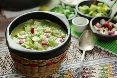 A bowl of green pozole verde topped with avocado and radish