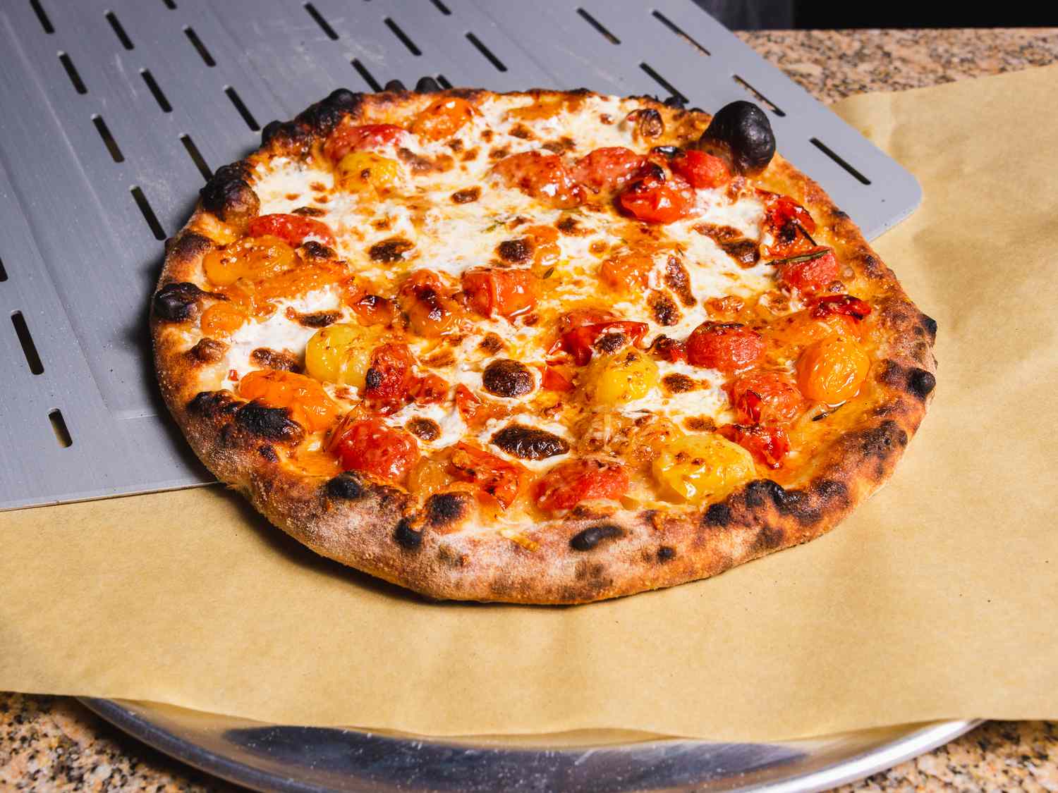 炸裂的樱桃番茄户外烤箱披萨正在从皮上滑到披萨盘上的羊皮纸上