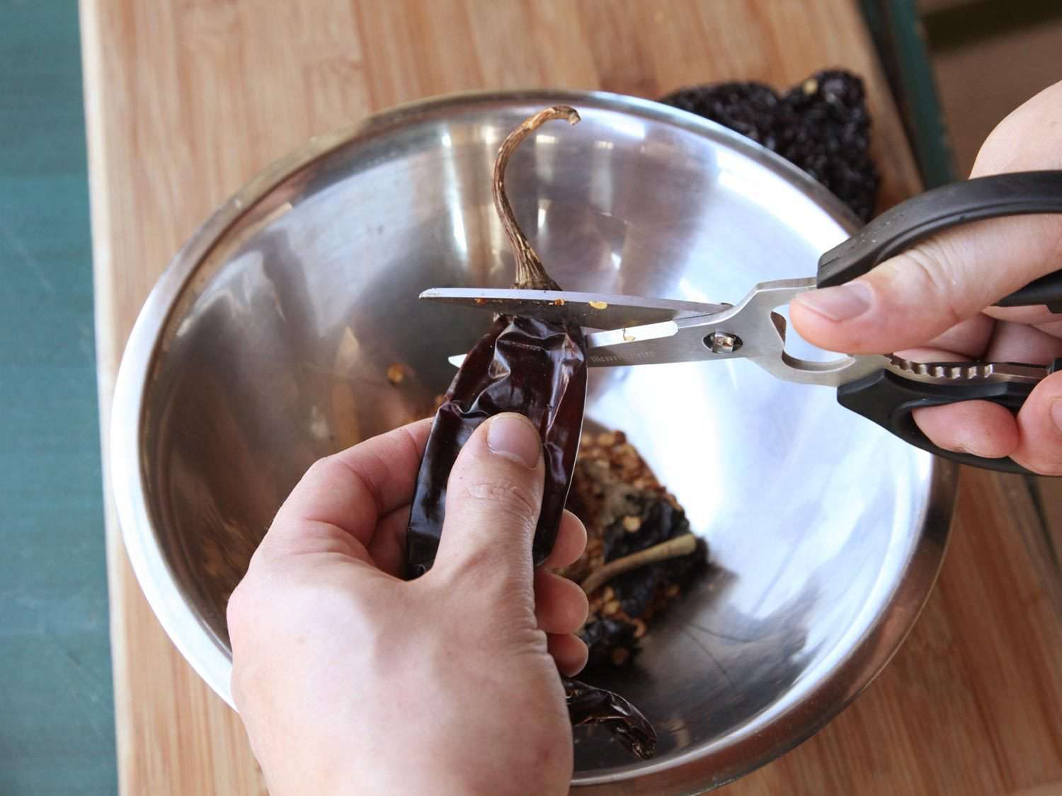 用剪刀把干辣椒的茎剪掉，放在盛有其他辣椒的金属碗上