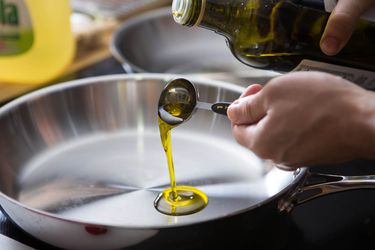Pouring a tablespoon of olive oil in a skillet to test if it's okay to use olive oil for high heat cooking.