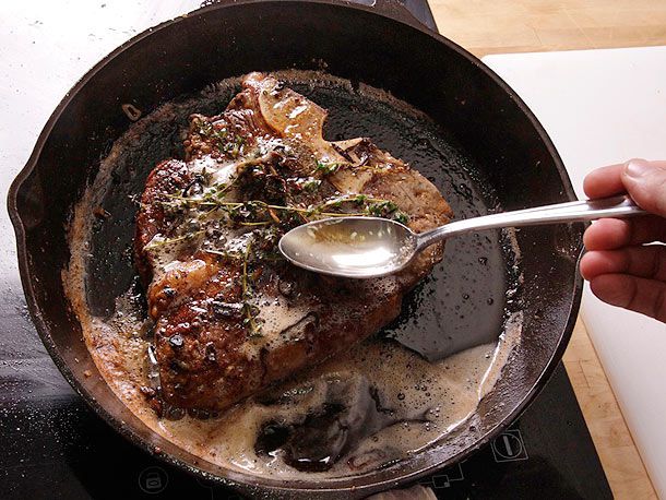 牛油和香草在热的铸铁煎锅里涂抹t骨牛排。