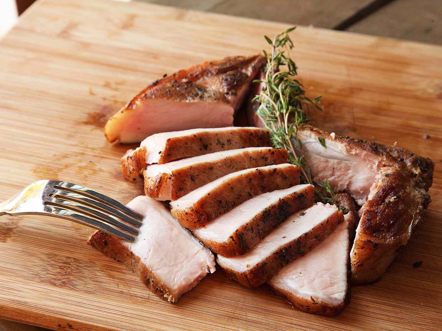 Sous vide bone-in pork chop, sliced, on a cutting board.