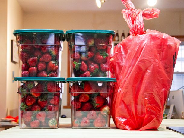 四个装满草莓的大cambro容器旁边是一个大的红色塑料杂货袋。