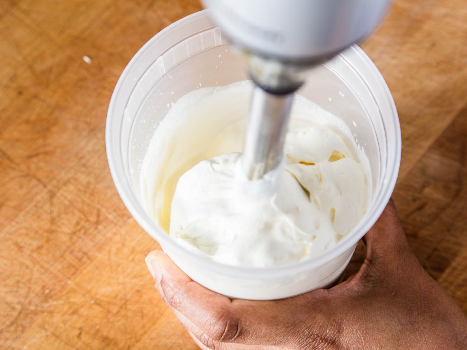 用一个浸入式搅拌器在透明塑料容器鲜奶油