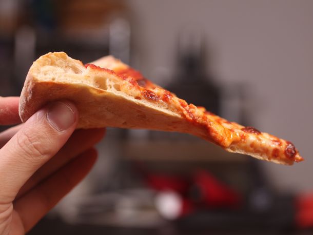 一只手举着一块自制的纽约式奶酪披萨。gydF4y2Ba