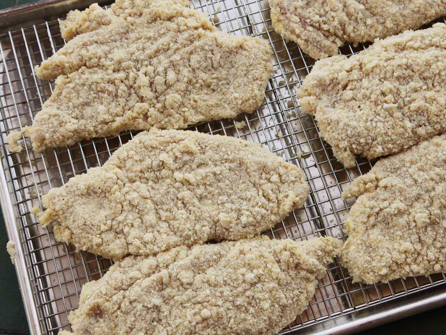 Breaded chicken breast laid out on a rack set over a rimmed baking sheet
