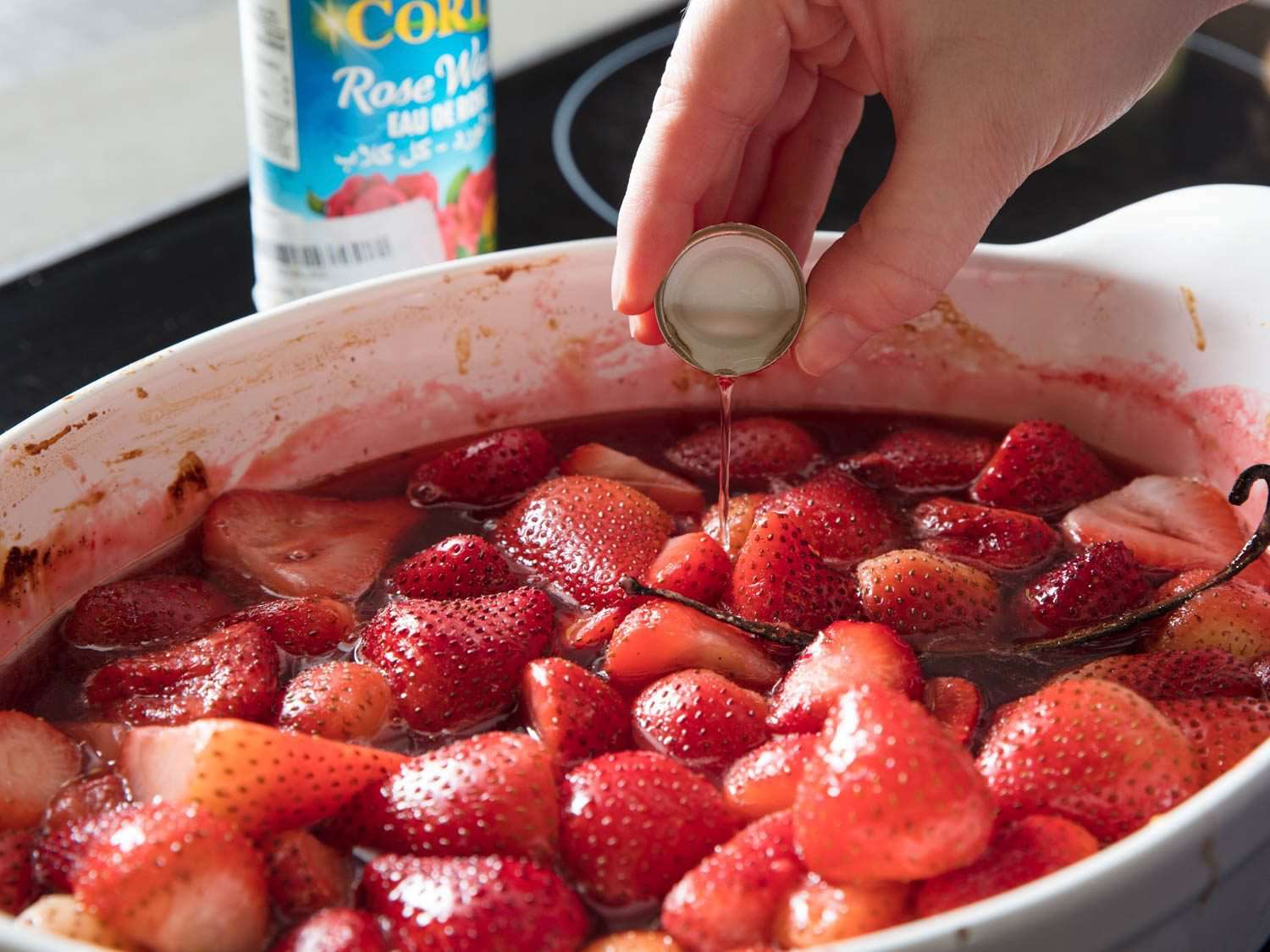 满满一帽的玫瑰水被放入盛满多汁草莓片的烤盘中