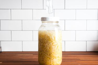 A jar full of sauerkraut on a countertop, with an airlock fixed on top to let gas out.