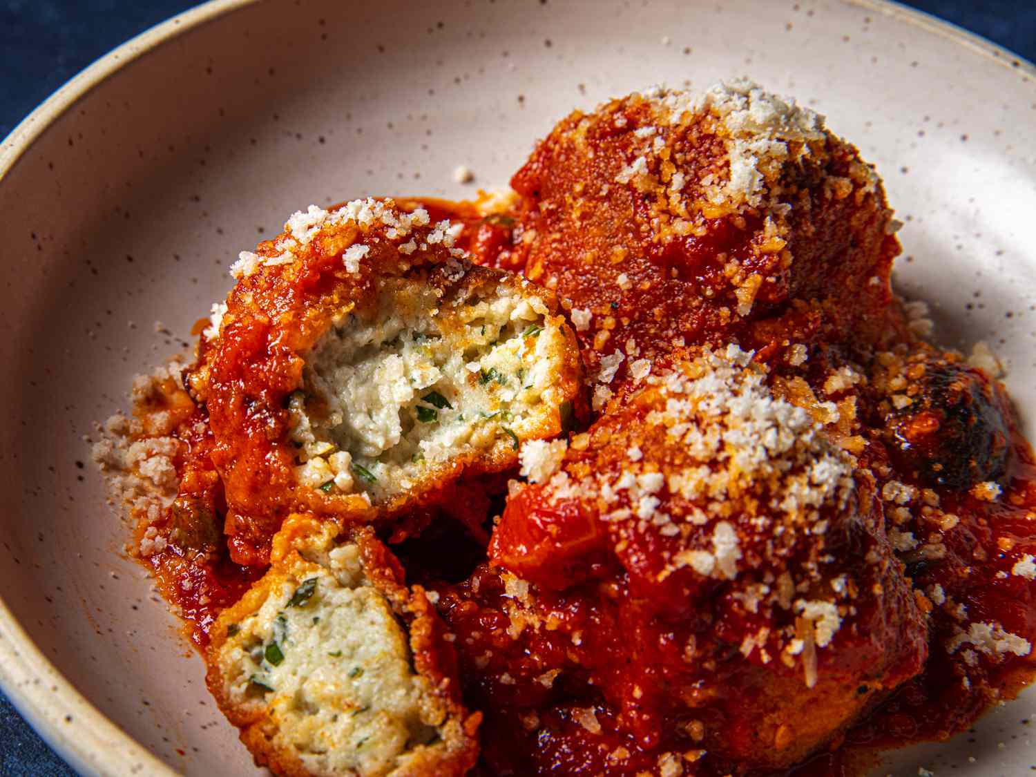Side angle view of a cut open ricotta ball in red sauce
