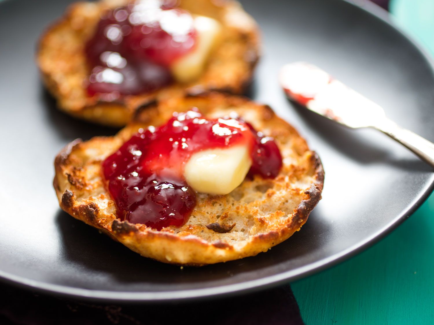把英式松饼放在深色盘子上，上面撒上几片黄油和红莓果酱。gydF4y2Ba