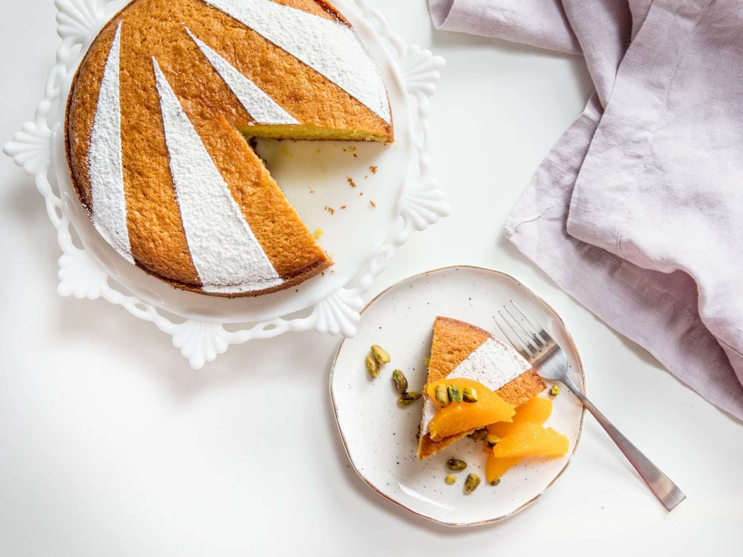 俯视图:盘子里放着一片橄榄油蛋糕，上面放着水果和坚果，旁边是蛋糕架上剩下的蛋糕