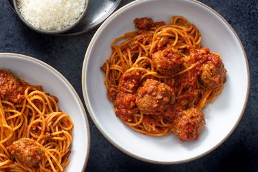 Two bowls of homemade spaghetti and meatballs with a dish of grated parmesan cheese next to them.