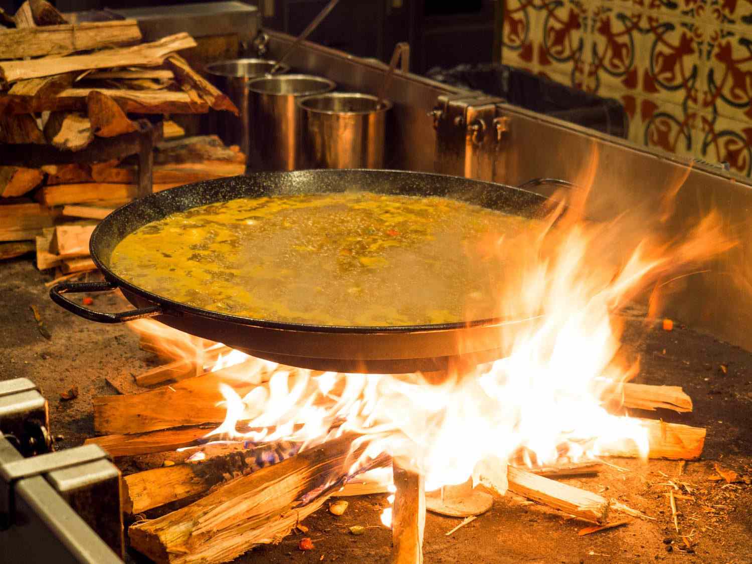 纽约梅尔卡多小西班牙餐厅的蔬菜海鲜饭，熊熊燃烧的柴火在大的海鲜饭锅周围喷出火焰。使用薄的木头可以让厨师很快地生起大火，然后也让它很快地熄灭。