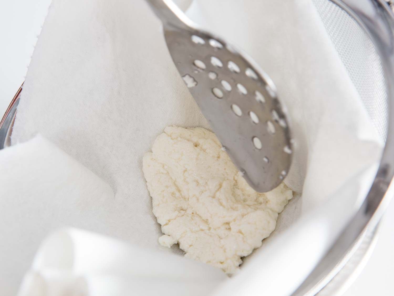 将一勺乳清干酪放入有纸巾衬里的滤网中沥干。