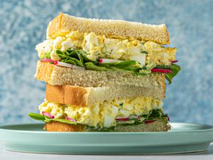 一个鸡蛋沙拉三明治,切成两半,两半一样堆在一起。包含鸡蛋沙拉三明治,奶油生菜,萝卜切成薄片。