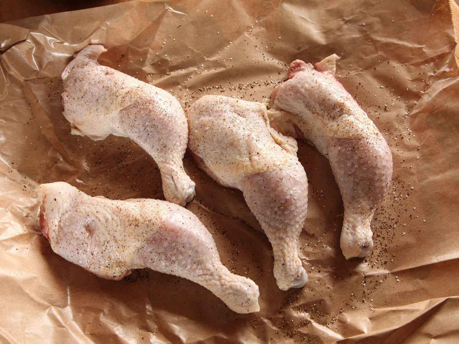 四只鸡腿放在一张皱巴巴的棕色蜡纸上，撒上黑胡椒。