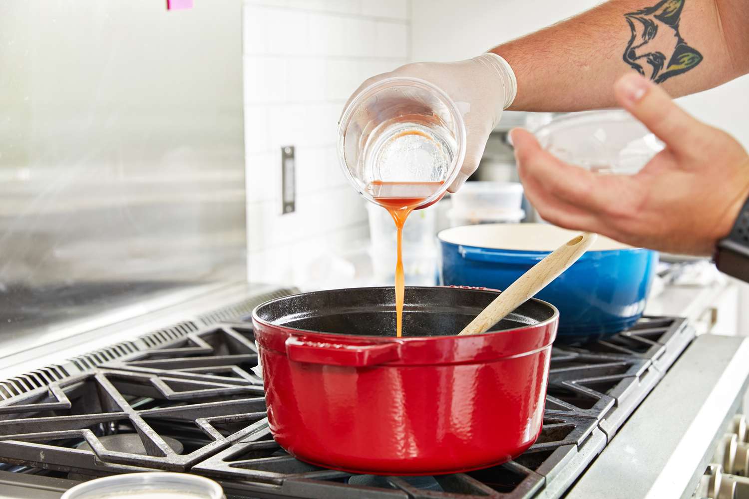 a hand pouring liquid into a red Dutch oven